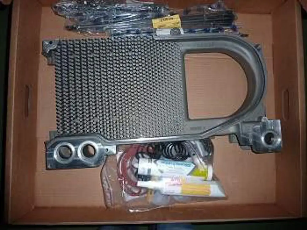 Mittelglied von Remeha in einer Kartonbox, bestehend aus einer metallischen Struktur mit Gittermuster und weiteren Komponenten in Klarsichtverpackungen.